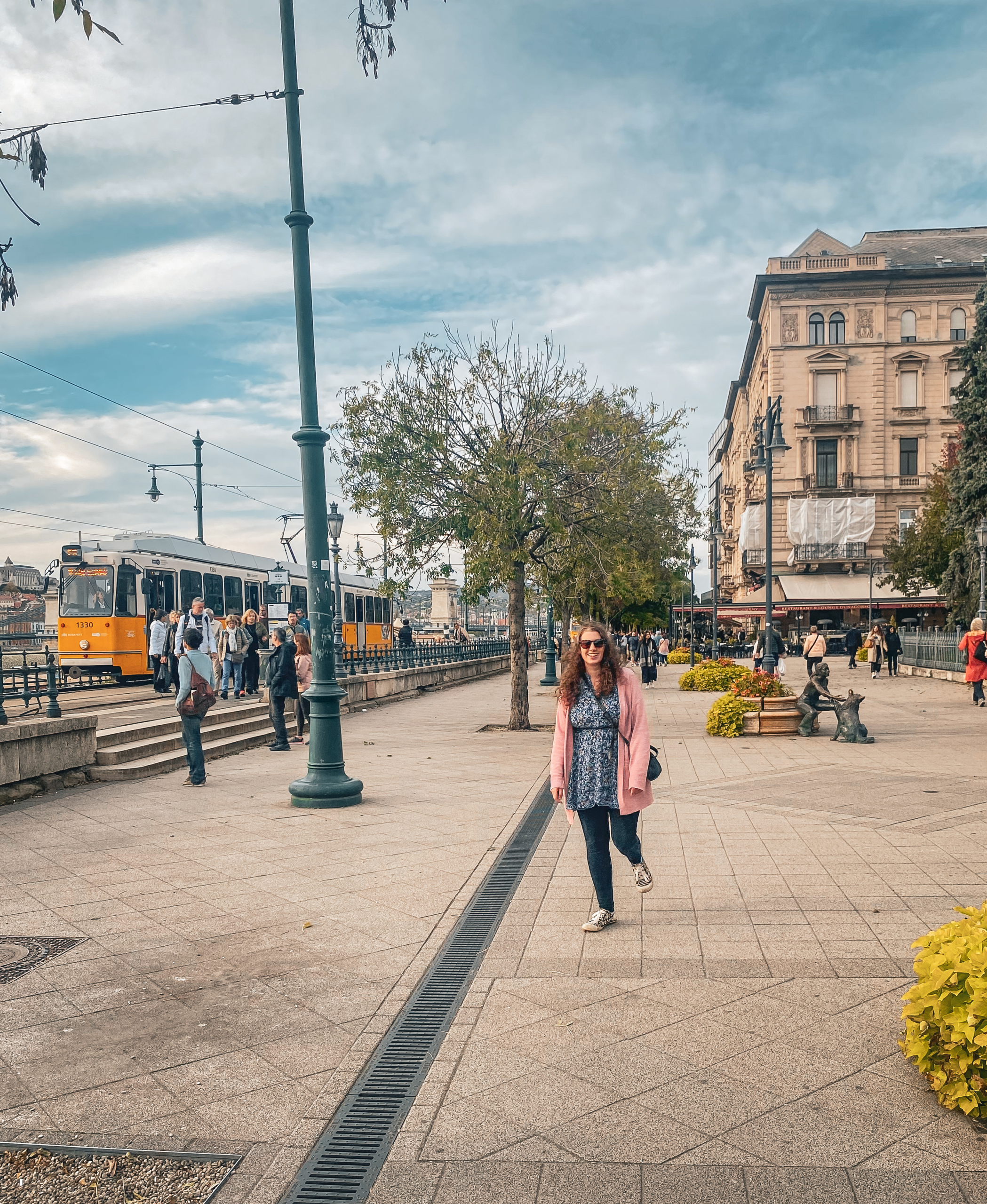 a woman stood in a street in Budapest, with a yellow tram coming past