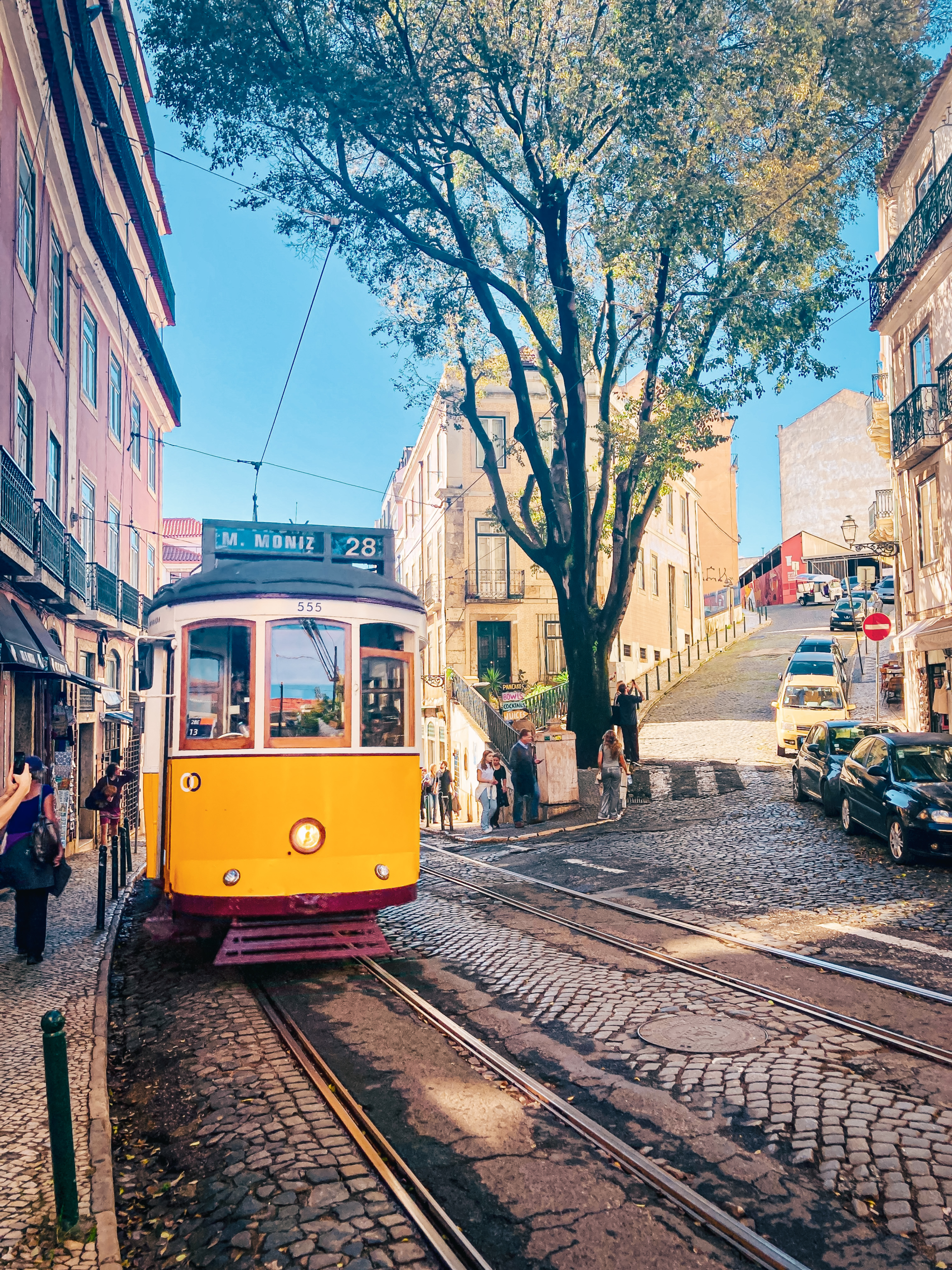 A yellow Tram 28 coming up a cobbled street in Lisbon, Portugal
